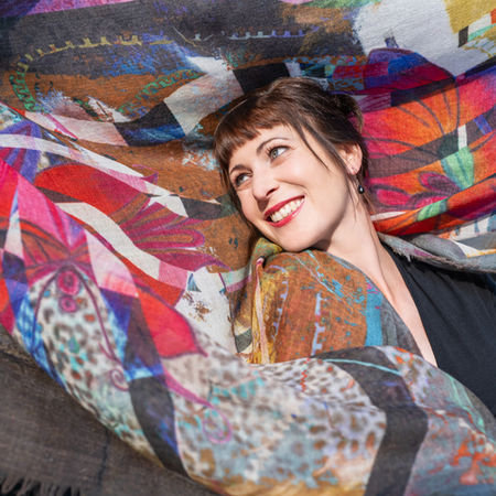 Lachende Frau posiert unter einem farbenfrohen Schal mit Mosaikmuster – lebensfrohe Portraitaufnahme mit Leichtigkeit.
