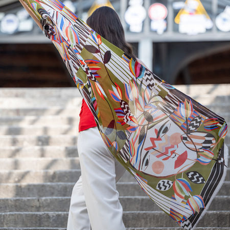 Dynamische Fashionaufnahme von hinten: Frau auf Treppe mit großem buntem Schal im Wind – Bewegung und Stil vereint.