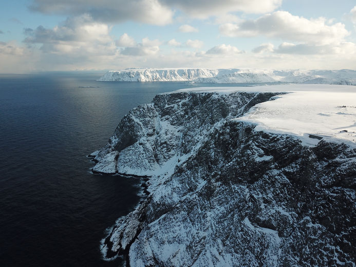Drohnenaufnahme von verschneiten Klippen an der arktischen Küste – dramatische Landschaft mit Blick auf das Meer und eisbedeckte Felsen.