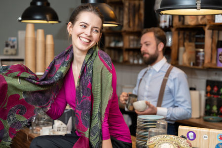 Fröhliche Frau in pinkem Oberteil trägt einen grünen Schal mit rotem Muster in einem gemütlichen Café – modisches Portrait mit Leichtigkeit.