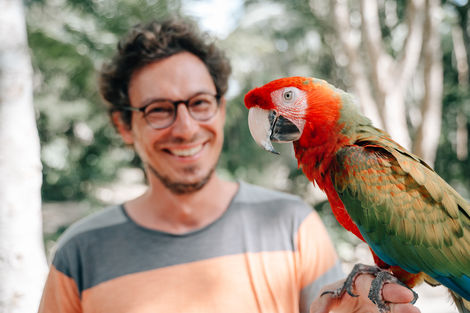 Lächelnder Mann hält fröhlich einen bunten Papagei auf dem Arm – Moment der Verbundenheit und Lebensfreude.