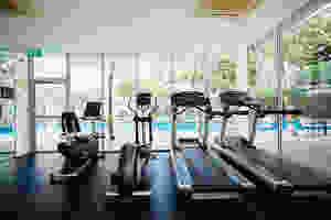A gym with two treadmills and other exercise machines by a pool are pictured.