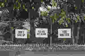 Signs on a fence that say "Don't give up," "You are not alone," and "You matter"