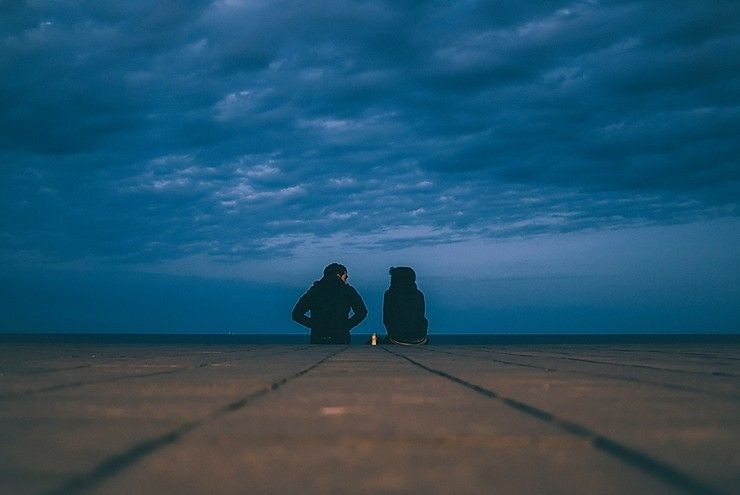 Two friends sit on an empty field and talk at night.
