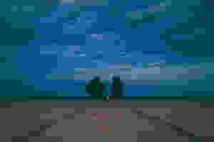 Two friends sit on an empty field and talk at night.