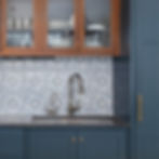 Blue kitchen with ornate patterned backsplash, stainless steel faucets, wooden cabinets, and glassware inside. Mood is elegant and tidy.