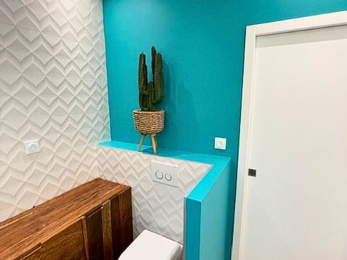 Couleurs salle de bain tendance 2025 : carrelage mural 3D blanc, mur turquoise et sol effet bois.
