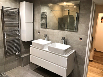 Salle de bain grise avec meuble double vasque suspendu et colonne salle de bain blanche, sèche-serviettes inox.