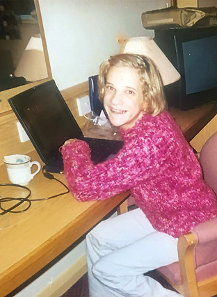 Claire, at a young age, sitting a desk, smiling toward the camera, midtype.