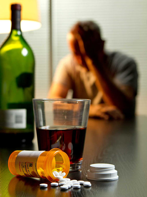 A man with his head in hands in front of a bottle of wine and drug