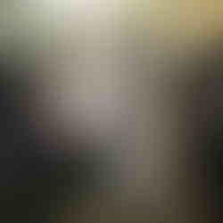 Varias prendas de ropa en tonos oscuros (gris, negro y beige) colgadas en perchas contra un fondo metálico brillante. Las prendas parecen ser camisas o chaquetas ligeras, y una de las prendas negras a la derecha tiene un diseño brillante decorativo.