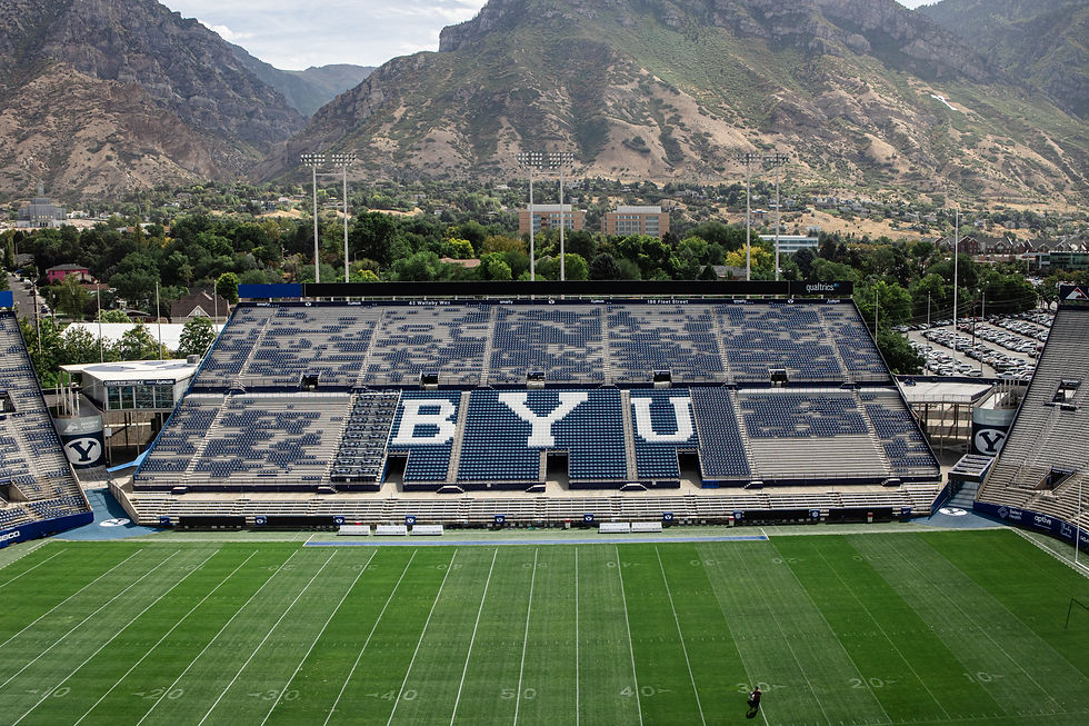 Empty BYU football stadium with blue seats spelling BYU, green field, and rugged mountains rising behind under a cloudy sky