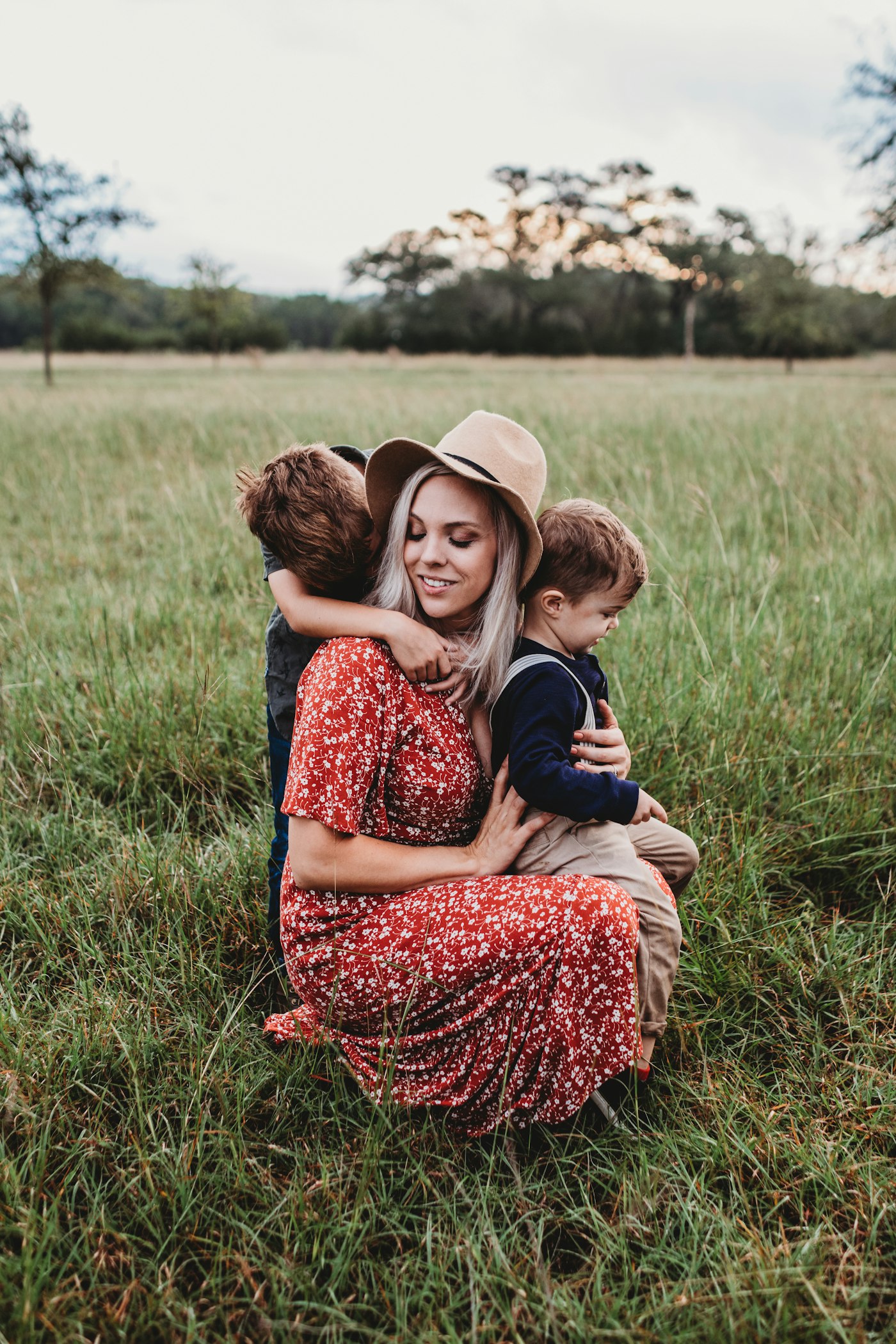 A mother hugging her two young children in a field