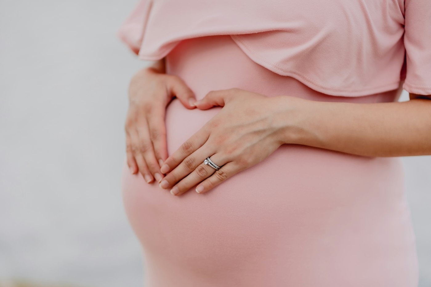 A pregnant woman in a pink dress resting her hands on her belly