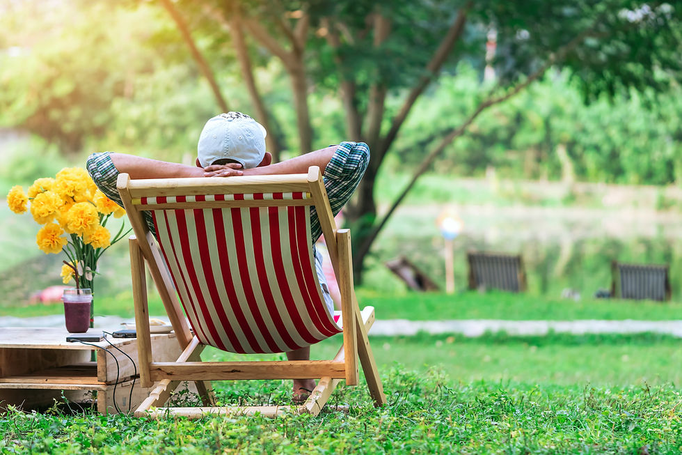 Back view of senior man with white hat sitting on garden chair and by the table in garden.