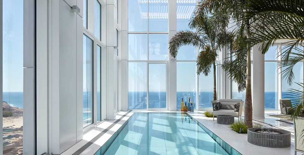פנטהאוס יוקרתי עם בריכת שחייה פנימית מוקפת חלונות זכוכית גבוהים, צמחייה טרופית ונוף פתוח לים