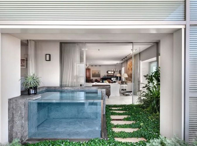 פנטהאוס מעוצב עם בריכת טבילה קטנה צמודה לחלל הפנים, מוקפת צמחייה ירוקה ושביל אבנים טבעי המחבר בין החוץ לפנים