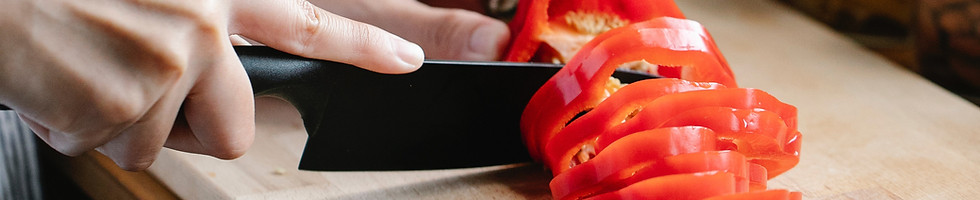 Main coupant un poivron rouge sur une planche à découper, nutrition et légumes en arrière-plan.