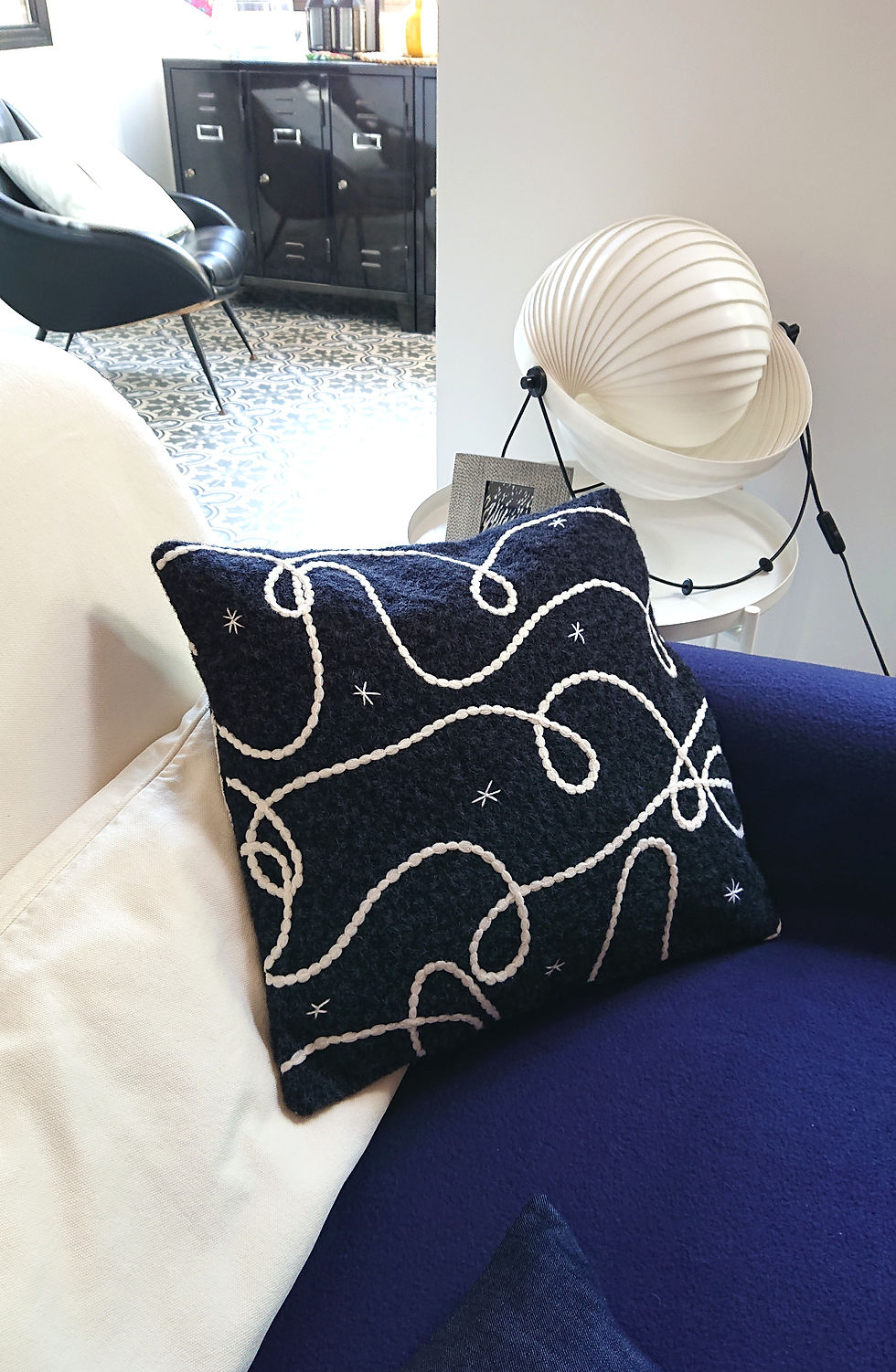 COSMO Housse de Coussin Déco en polaire graphique, photographiée sur un e assise bleu vif.