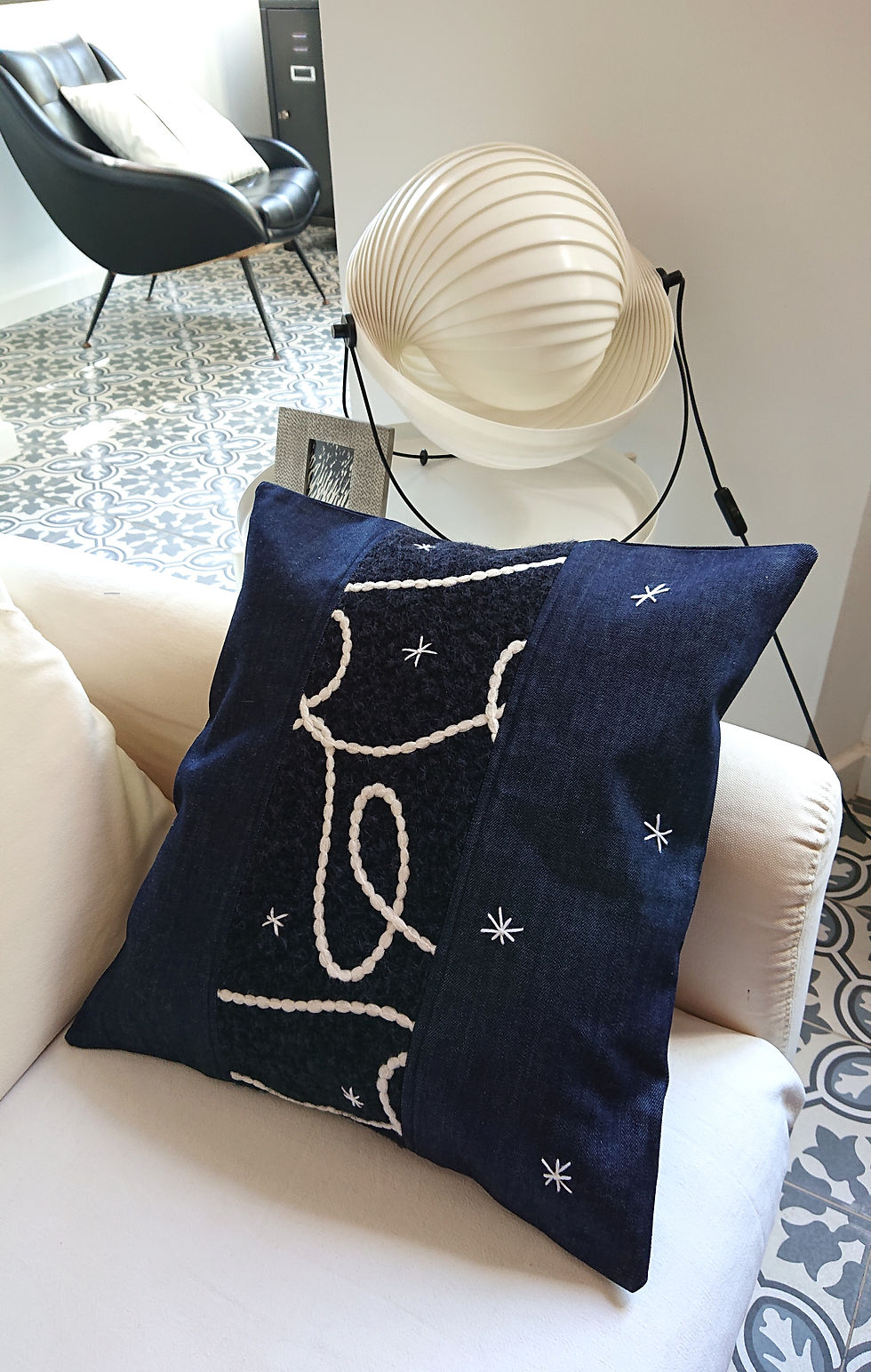 CALLISTO Housse de coussin Déco en jean brut et polaire, présentée sur un canapé écru.