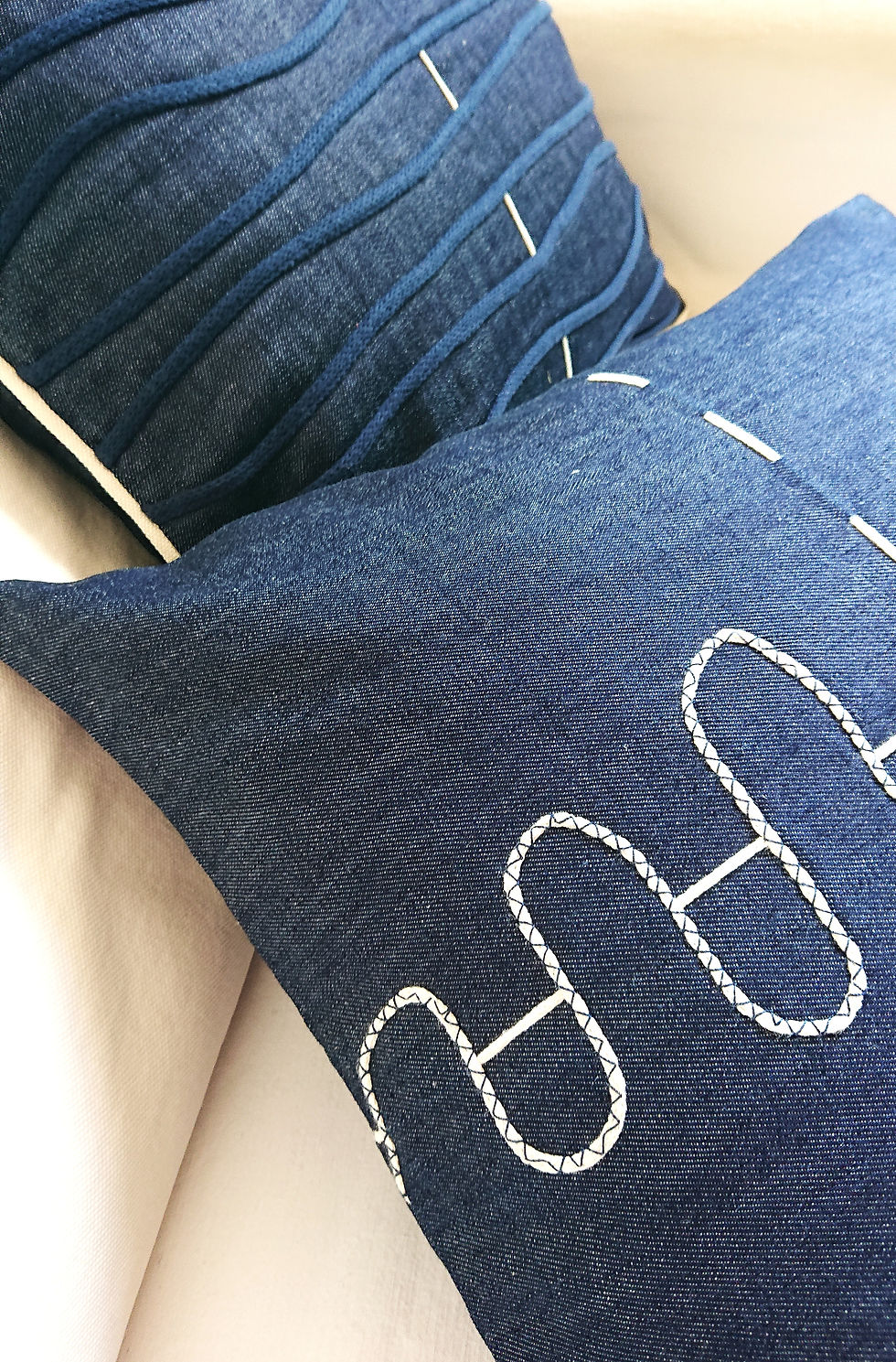 CELESTO Housse de coussin Déco jean brut, présentée sur un canapé écru avec un autre modèle