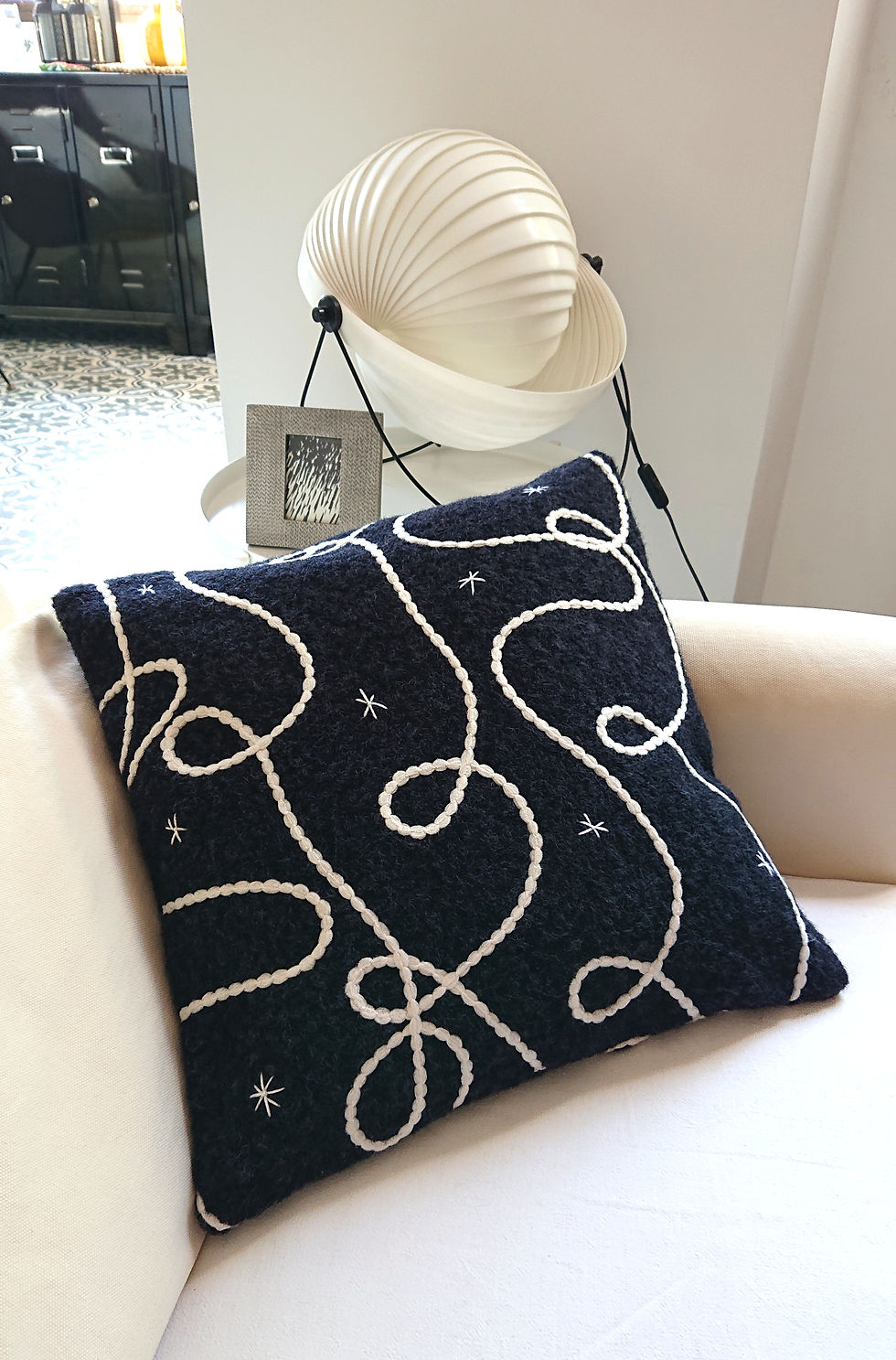 COSMO Housse de Coussin Déco en polaire graphique, photographiée sur un canapé écru.