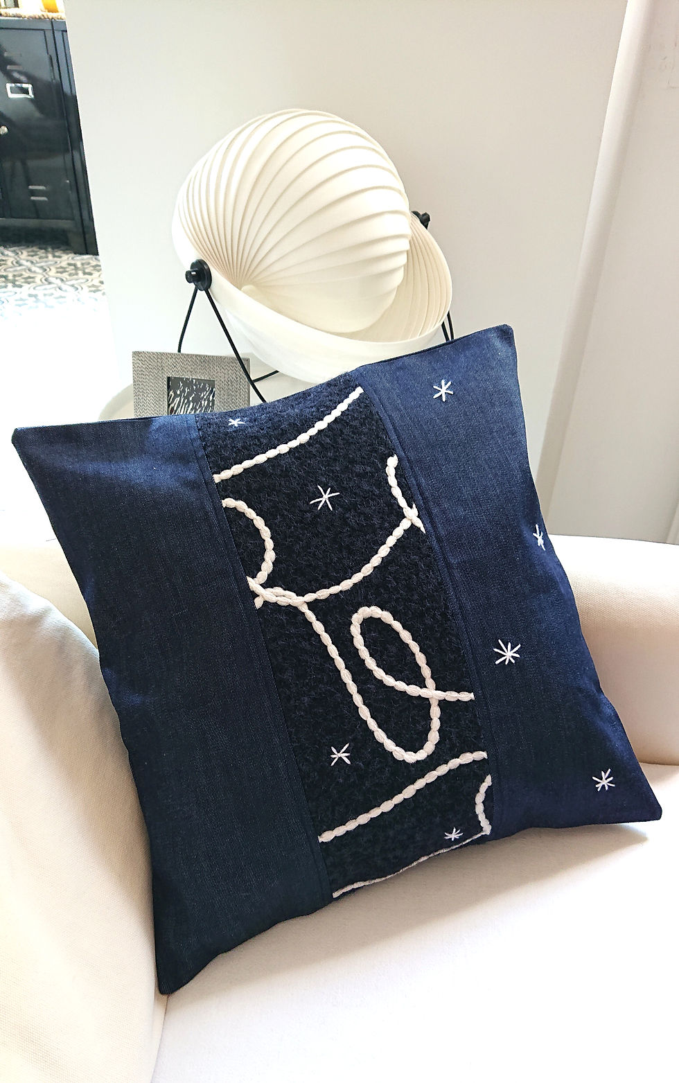 CALLISTO Housse de coussin Déco en jean brut et polaire, présentée sur un canapé écru.