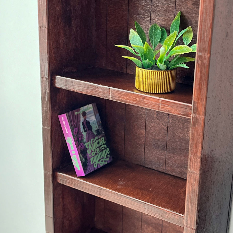 Close-up of handcrafted 1:6 scale wooden doll bookcase with dark stained shelves, miniature books and decorative plant