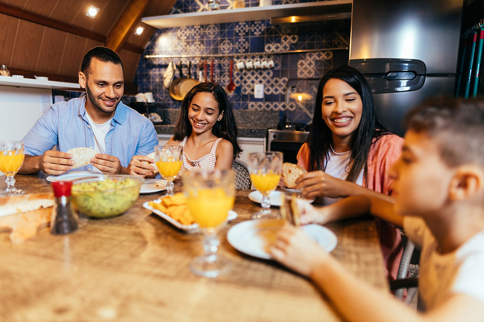 A latino family (mom, dad, sister, and brother) sitting down at the dinner table, smiling and eating dinner.