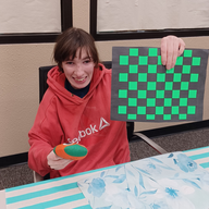Member proudly holding completed paper weaving craft project