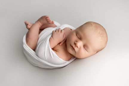 En nyfødt baby som ligger på et hvitt teppe under en nyfødtfoto