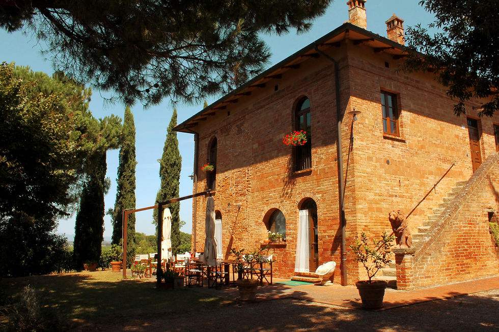 Brick villa in sunny Italian countryside, surrounded by trees. Outdoor tables, chairs, and umbrellas enhance the inviting, peaceful atmosphere.