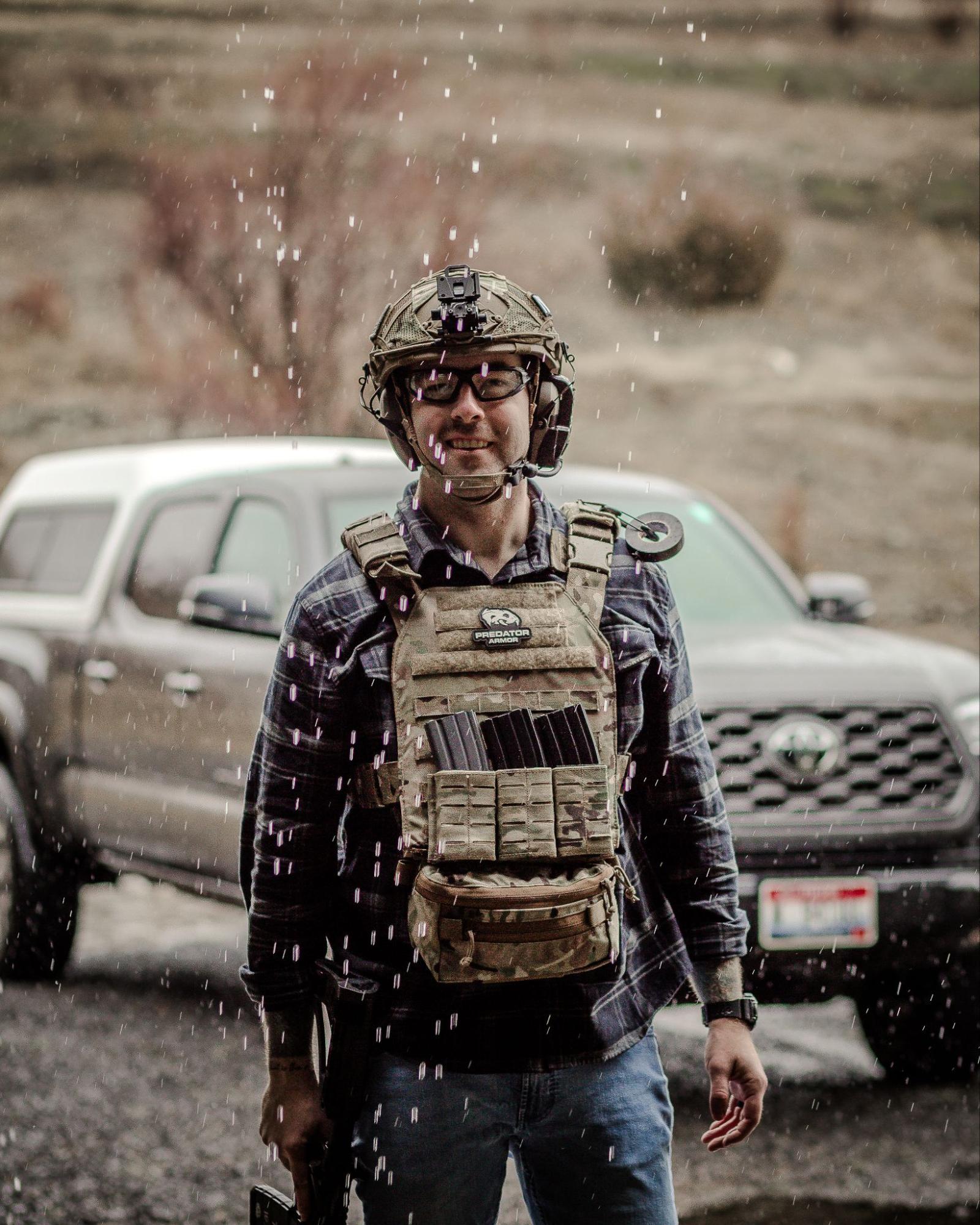 Man in tactical gear and helmet stands in front of a parked truck