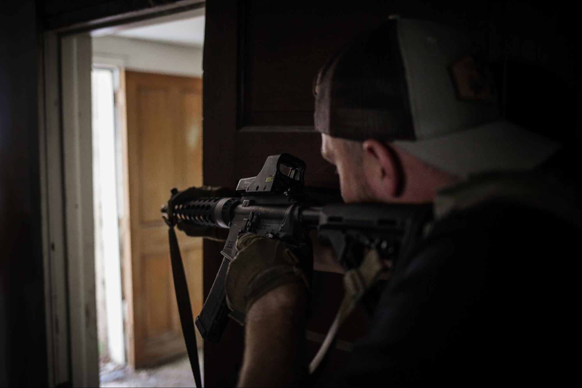 Man aims rifle inside dark room toward doorway