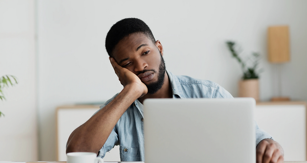 A tired man sitting at his desk, leaning on his hand while looking at his laptop, illustrating fatigue, burnout, or feeling mentally drained.