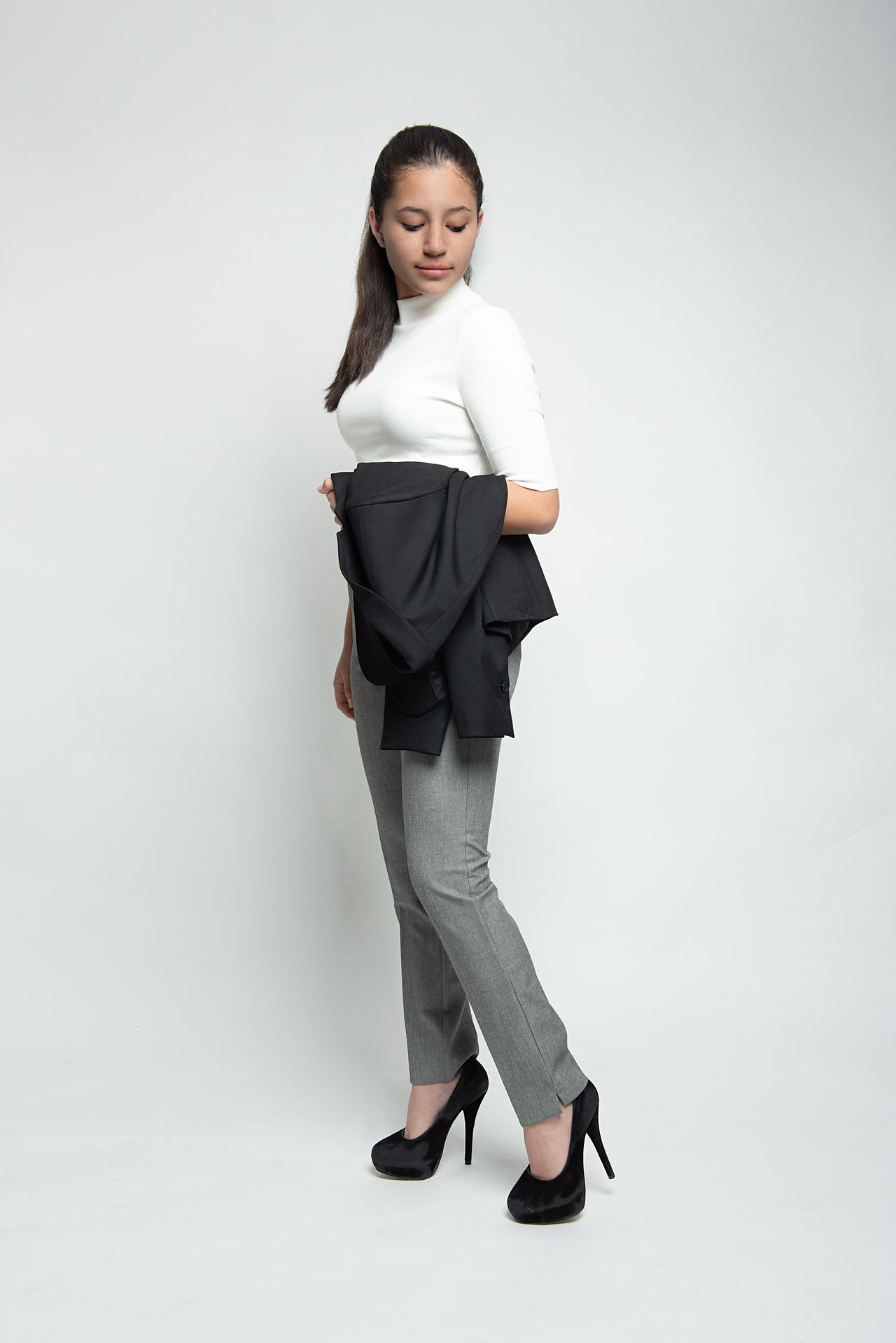 Full length studio portrait photographed on white background in a mid walk position, wearing jeans, black high heels and white polo top holding black jacket
