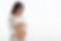 Happy young pregnant woman in comfortable homewear standing next to window at home, lookin