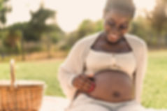 African woman caressing her pregnant belly while doing a picnic in park - Maternity lifest