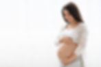 Happy young pregnant woman in comfortable homewear standing next to window at home, lookin