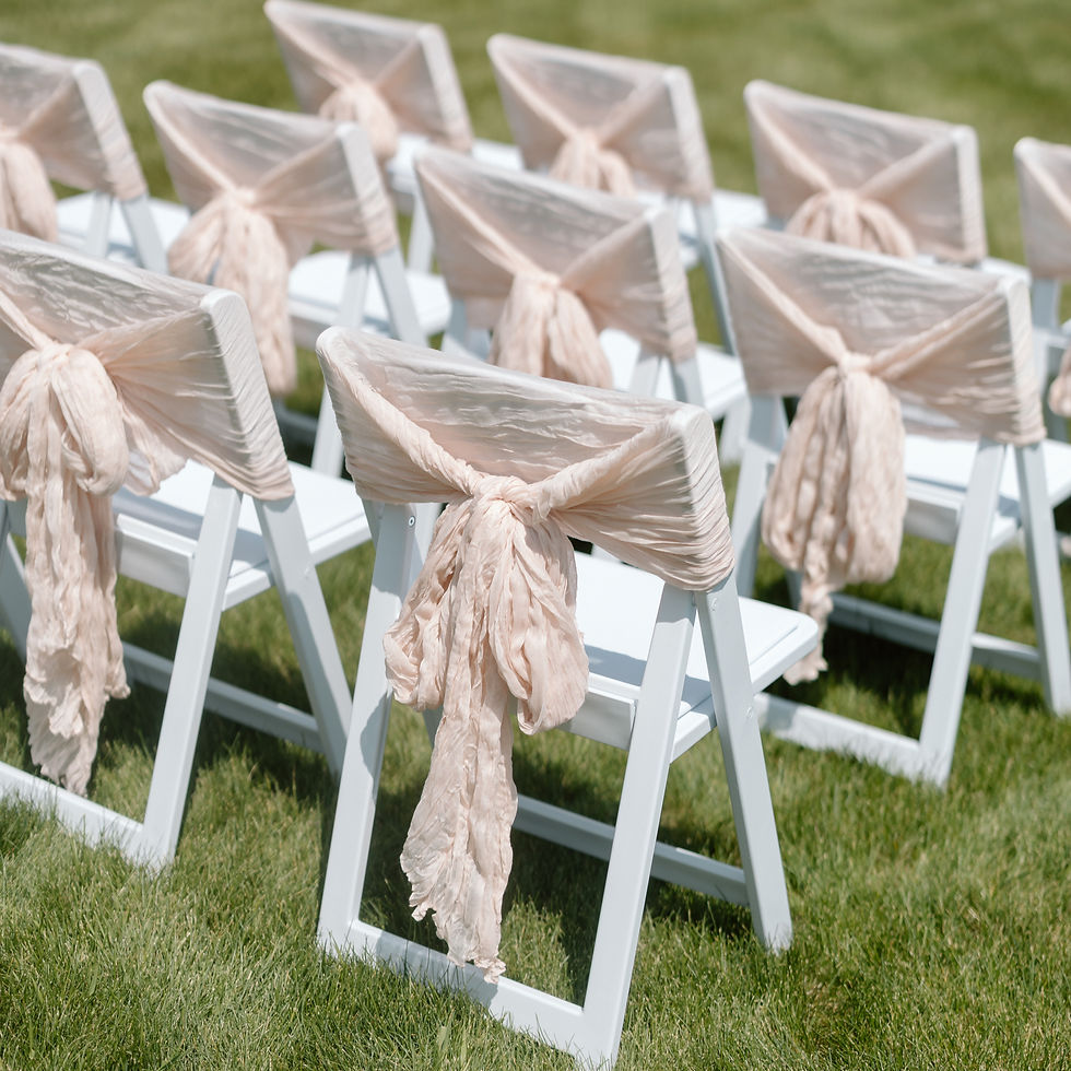 White folding chairs styled with blush cheesecloth chair sashes for an elegant outdoor wedding ceremony in Lloydminster.