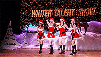 a moving image of four women in Santa costumes dancing forward on a stage in unison. The background reads "Winter talent Show" and has a winter scene with snow, reindeers and a Christmas tree.