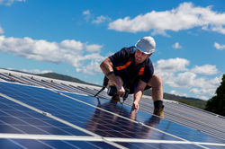Solar panel technician with drill installing solar panels on roof on a sunny day.jpg