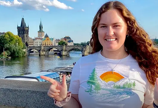 girl posing in front of eurpoean bridge holding up finger gun