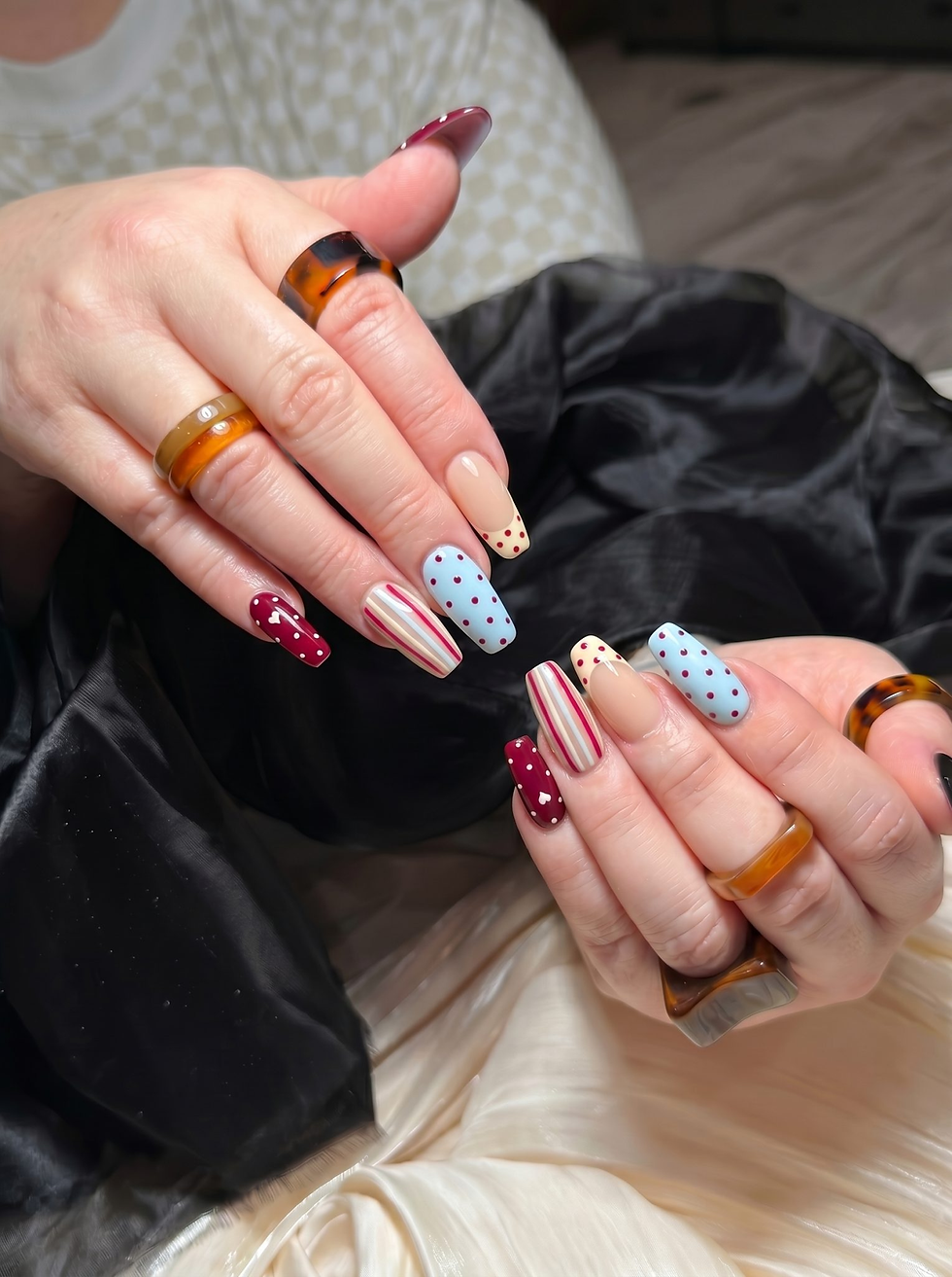 Close-up of two hands showing colorful patterned manicured nails and tortoiseshell rings on a satin blanket.