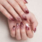 A close-up of hands with glossy burgundy and nude floral nail art featuring 3D flower designs, gold accents, and almond-shaped nails.