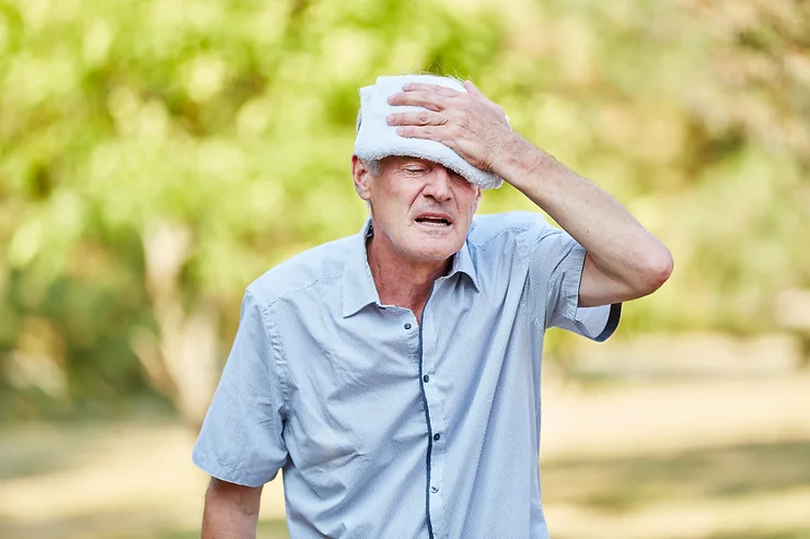 Elderly man outside in the heat holding flannel on his head