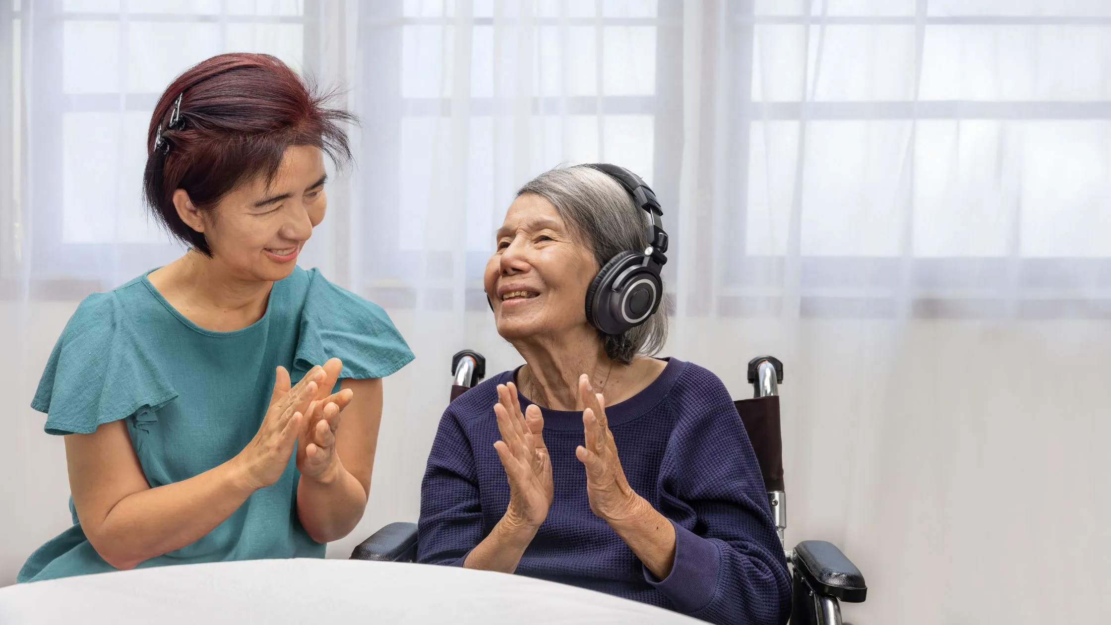 Elderly woman in wheelchair with headphones on listening to music with her home carer