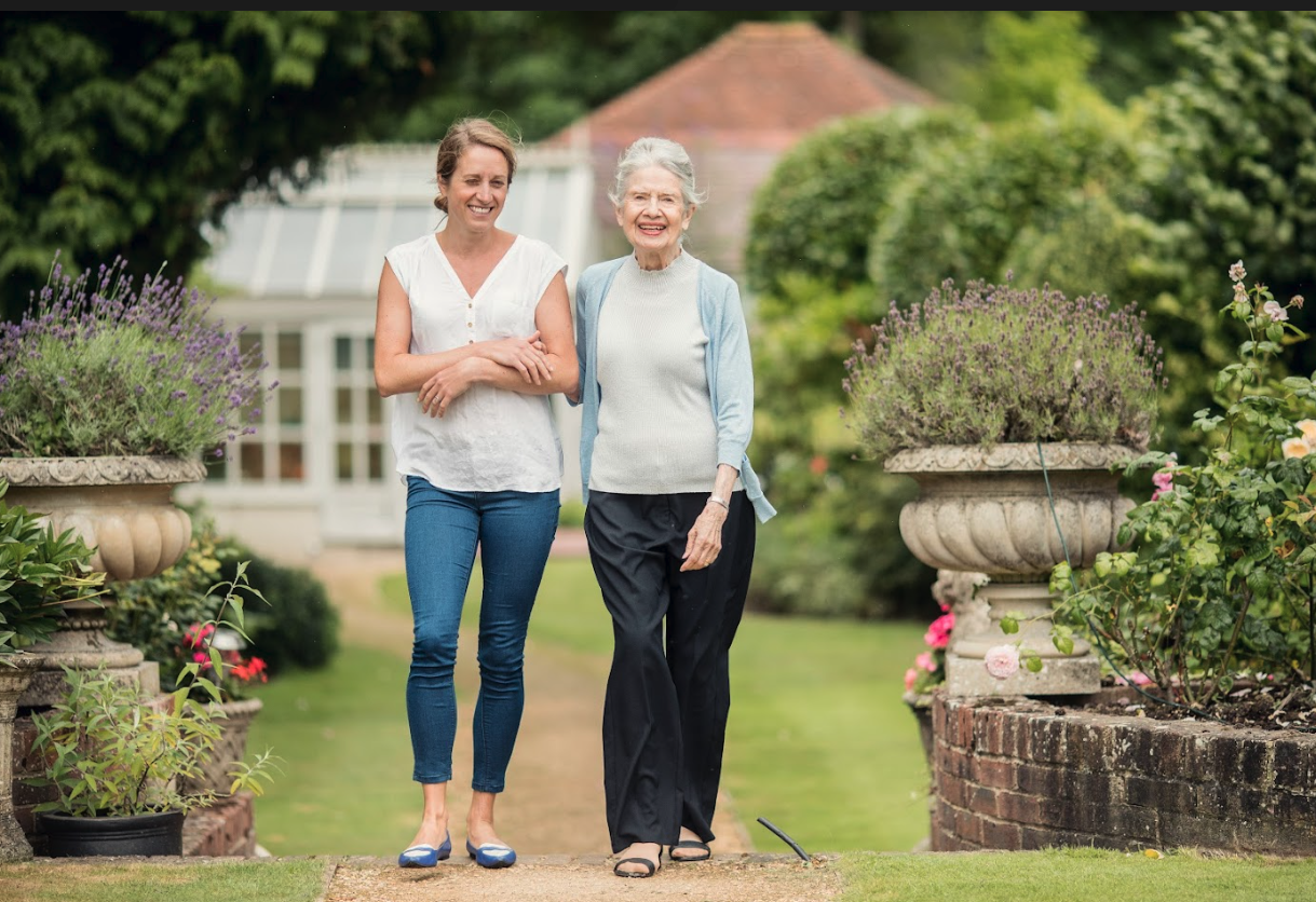 Home carer with elderly lady in pretty garden walking together