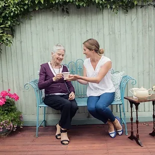 Elderly lady sat in garden drinking tea with home carer