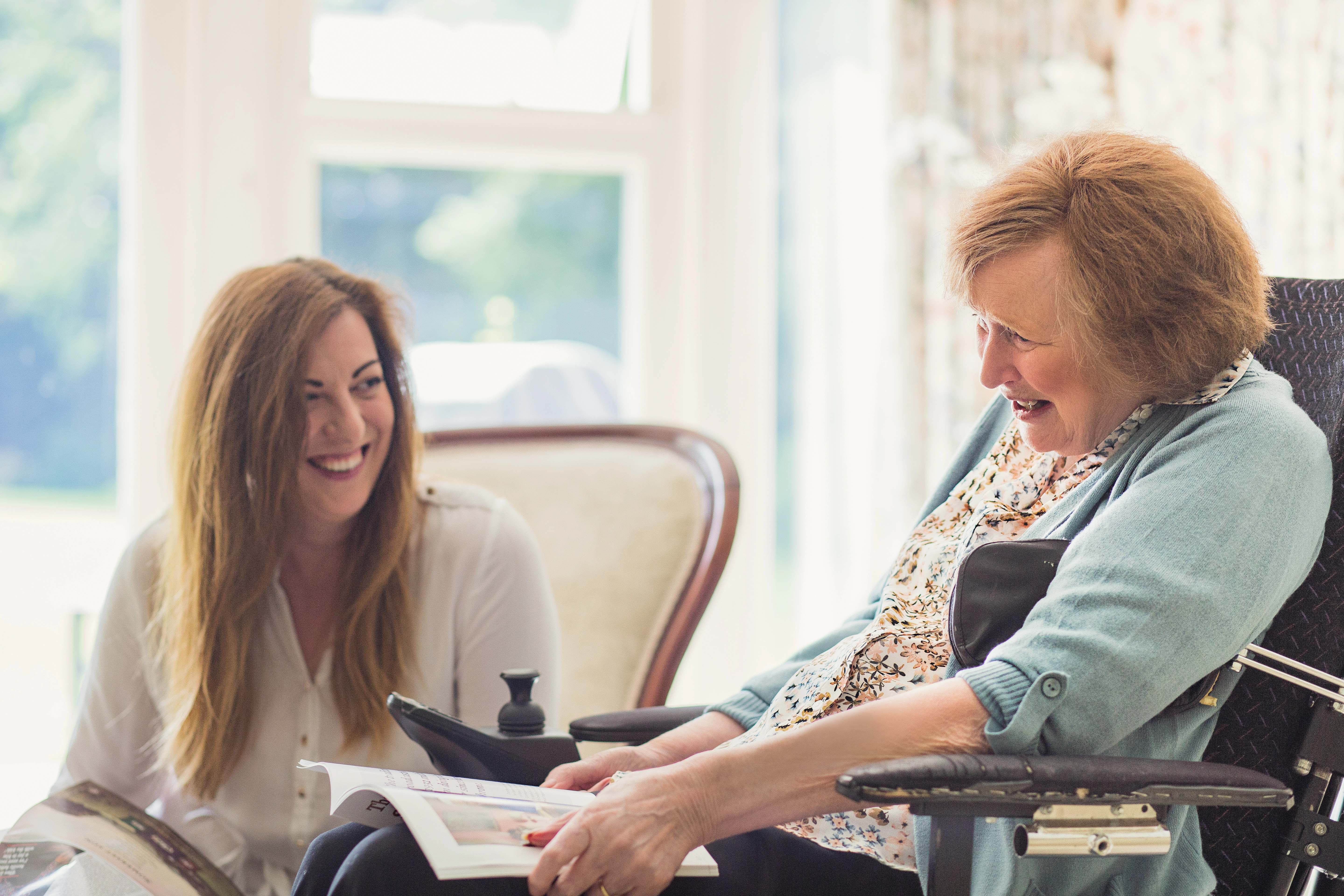 Home carer with multiple sclerosis client at home smiling and reading